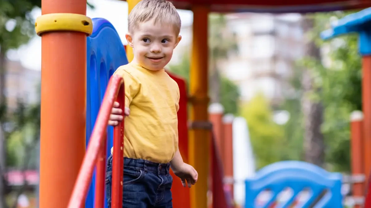 Criança com Síndrome de Down brincando no parquinho - desenvolvimento social e inclusão
